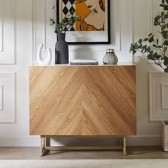 a wooden cabinet with vases on it in front of a painting and potted plant