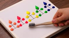 a child's hand holding a wooden brush over a white board with colorful candies on it