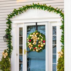 a christmas wreath on the front door of a house with holiday decorations hanging from it