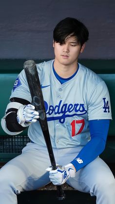 a baseball player sitting in the dugout holding a bat