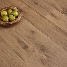 a bowl filled with green apples on top of a wooden floor