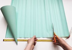 two hands holding scissors and measuring the length of a sheet of green paper with a tape on it