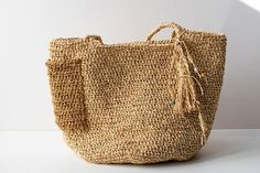 a woven straw bag with tassels on the handles and bottom, sitting on a white surface