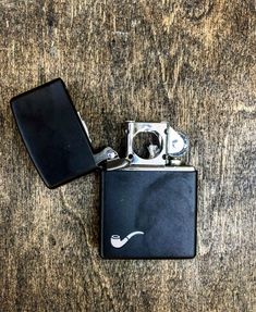 a black zippo lighter sitting on top of a wooden table next to a cell phone