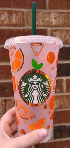 a hand holding up a pink starbucks cup with oranges and green leaves on it