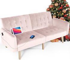 a pink couch sitting next to a christmas tree with a laptop on it's back