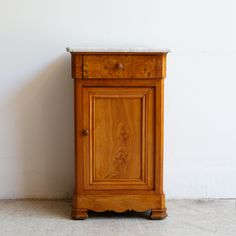 an old wooden cabinet with marble top in front of a white wall and tile floor