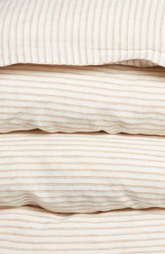 three pillows stacked on top of each other in front of a white bed with striped sheets