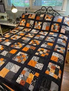 a bed with a black and orange quilt on it's headboard next to a window