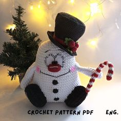 a crochet snowman sitting next to a christmas tree