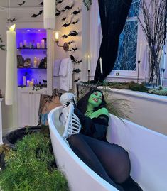 a woman with green makeup sitting in a bathtub filled with fake plants and candles