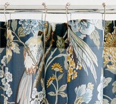 the curtains are decorated with flowers and birds on blue floral fabric, hanging from metal rods