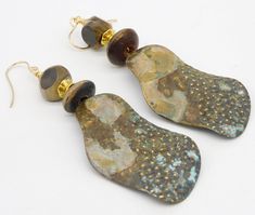 1 Pair Available! Pics do not do justice....long wavy handforged brass drops have been textured with hammer and patinated.  Raised dots are brushed to reveal shiny gold metal..  The colors are subtle....a little speck of blue, some golden tan, gray-blue, dark brownlovely patterns created by patination.  I have topped the statement sized drops with stack of handcarved horn beads separated by GP  bead. Earrings are a tad over 3 1/2 inches in length, including my handmade 14KT GF French wires.  Lig Hand Forged Brass Earrings In Brown, Rustic Gold Dangle Jewelry, Earthy Bronze Brass Earrings, Rustic Gold Drop Earrings, Artisan Brass Earrings With Patina, Rustic Brass Earrings With Patina, Rustic Gold Brass Earrings, Rustic Gold Metal Earrings, Golden Tan