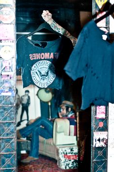 a man with tattoos on his arm standing in front of a mirror and holding onto a t - shirt