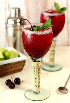 two glasses filled with red liquid and topped with mint sprinkles on a table