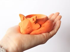 a hand holding an orange toy with a sleeping fox on it's back,