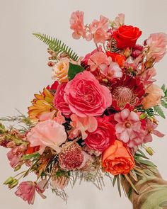 a bouquet of flowers is being held up by someone's hand in front of a white wall