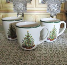 three coffee mugs sitting on top of a table next to each other with christmas trees painted on them