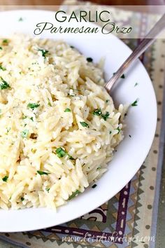 a white plate topped with rice covered in parmesan cheese and garnished with herbs