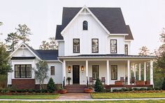 a large white house with black roof and two story front porch, surrounded by greenery