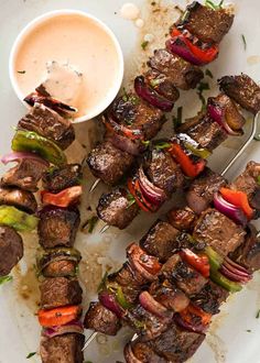 skewers of meat and vegetables on a plate with dipping sauce