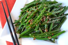 green beans with sesame seeds and seasoning on a white plate next to chopsticks