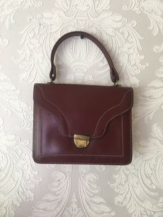 "Vintage cognac brown vegan leather handbag. Classic retro 70s design bag with golden tone closure. Accessories european quality. Women detective style purse. Inside red textile lining and 2 open way pockets. condition: normal condition. The closure is shabby. The closure works well. The red lining has some spots. measurements: width 24 cm / 9.4\" in height without handle 19 cm / 7.4\" in handle length 33 cm / 13\" in" Retro Brown Square Shoulder Bag, Retro Brown Satchel Shoulder Bag, Retro Office Satchel With Gold-tone Hardware, Retro Shoulder Bag With Gold-tone Hardware For Office, Retro Business Shoulder Bag With Gold-tone Hardware, Brown Business Satchel With Handles, Vintage Brown Bag With Hasp Closure, Vintage Brown Bags With Hasp Closure, Retro Brown Satchel With Hasp Closure