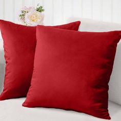 two red pillows sitting on top of a white couch next to a vase with flowers