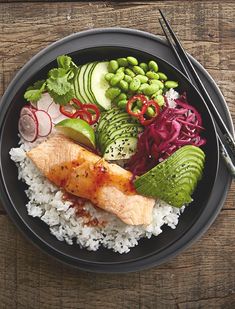 a black plate topped with rice, fish and veggies next to chopsticks