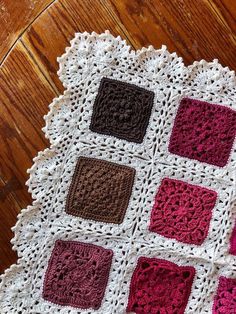 a crocheted blanket with squares on top of it sitting on a wooden floor