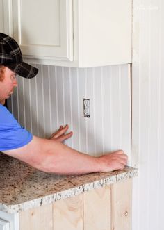 a man in blue shirt and black hat working on kitchen counter top with white cabinets