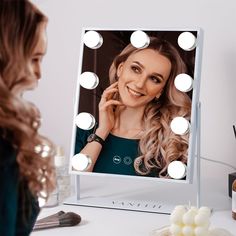 a woman is looking at her reflection in the mirror with lights around her and smiling