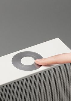 a person's finger is pressing the button on a white speaker with grey background