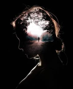 a person standing in the dark with their head turned to look at an image of a tree