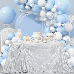 a table topped with cake and balloons next to a white wall covered in blue and silver decorations