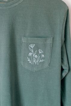 a green shirt with white flowers on the front and back pocket, hanging from a hanger