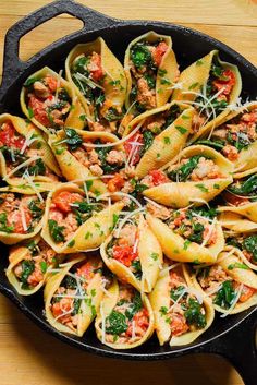 a skillet filled with pasta, meat and spinach on top of a wooden table