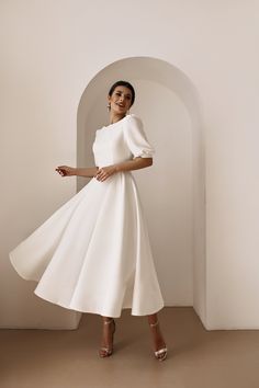 a woman wearing a white dress and heels standing in front of a wall with arches