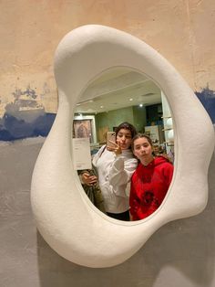 two women taking a selfie in a mirror on the wall at an art gallery