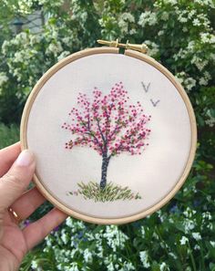 a person holding up a small embroideryed tree with pink flowers on it's branches