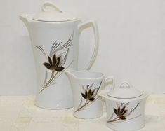 three pieces of white porcelain with black flowers on them, one pitcher and two cups