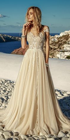 a woman in a wedding dress standing on rocks near the ocean with her hand to her face