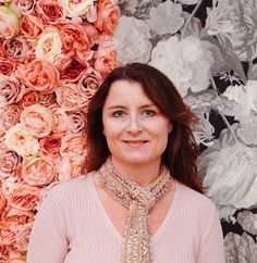 a woman standing in front of a wall with flowers on it and wearing a scarf around her neck