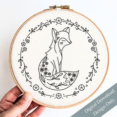 a hand holding a embroidery hoop with a fox on it