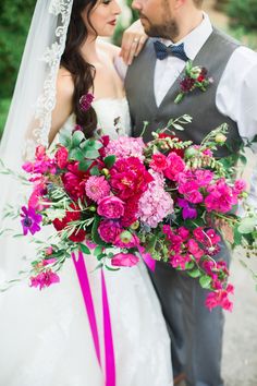 a bride and groom standing next to each other in front of some trees with pink flowers