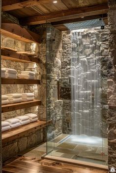 a bathroom with stone walls and a waterfall in the shower area, along with wooden shelves filled with white towels