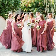 a group of women standing next to each other in long dresses and holding bouquets