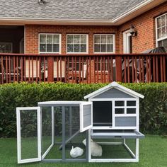 a chicken coop with a white ball in the grass and a red brick house behind it