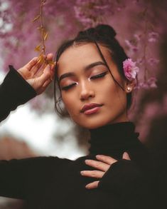 a woman with her hands on her head and flowers in her hair, standing under a cherry blossom tree