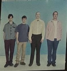 an old photo of four men standing next to each other in front of a blue wall